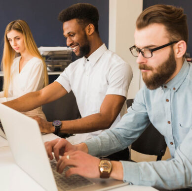 Group of young professionals working on laptops in an office, collaborating and smiling while focusing on their tasks