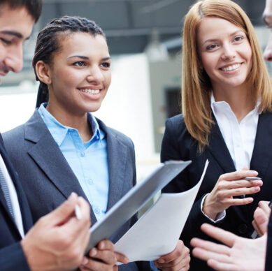 Group of business professionals smiling and discussing work while holding documents during a meeting