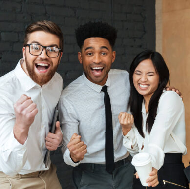 Three cheerful business colleagues celebrating success together, smiling and showing excitement in an office setting