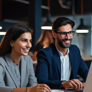 Two colleagues smiling and working together on a laptop in a warmly lit office setting