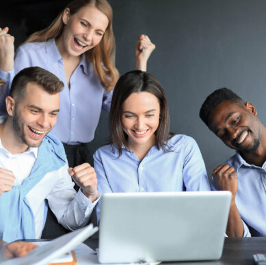 Group of happy coworkers celebrating success while looking at a laptop together in an office setting