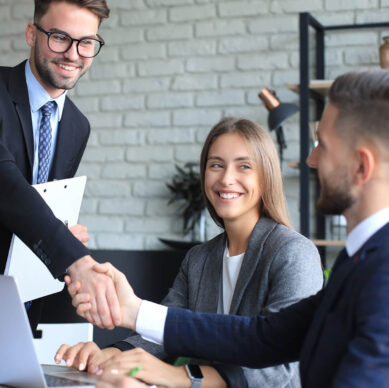 Business professionals in formal attire smiling and shaking hands during a meeting in a modern office