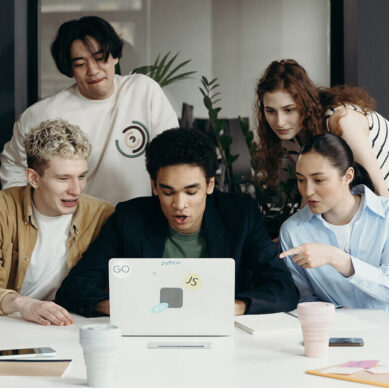 Group of young professionals gathered around a laptop, collaborating and discussing ideas in a modern office setting