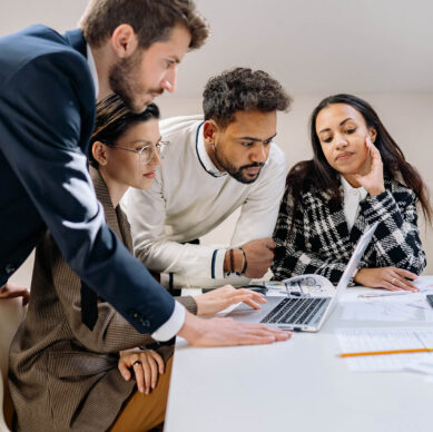 Team of professionals collaborating over a laptop, analyzing documents and discussing work ideas in a bright modern office