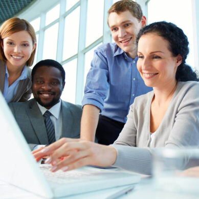 Group of business professionals smiling and collaborating while working on a laptop in a bright modern office