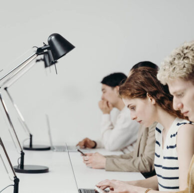 Group of young professionals working on laptops at a long white desk with modern black desk lamps in a bright minimalist office