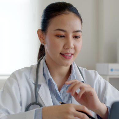 A female doctor is smiling and talking while working on her laptop