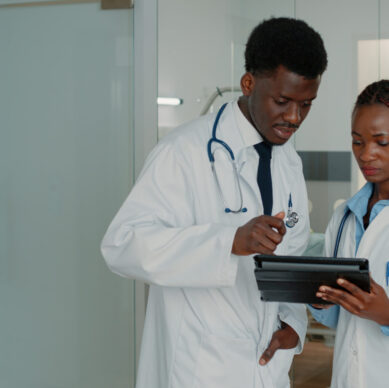 Doctors using digital tablet to treat patient with sickness in hospital ward. Medical team of specialists looking at device display to find healthcare treatment against disease.